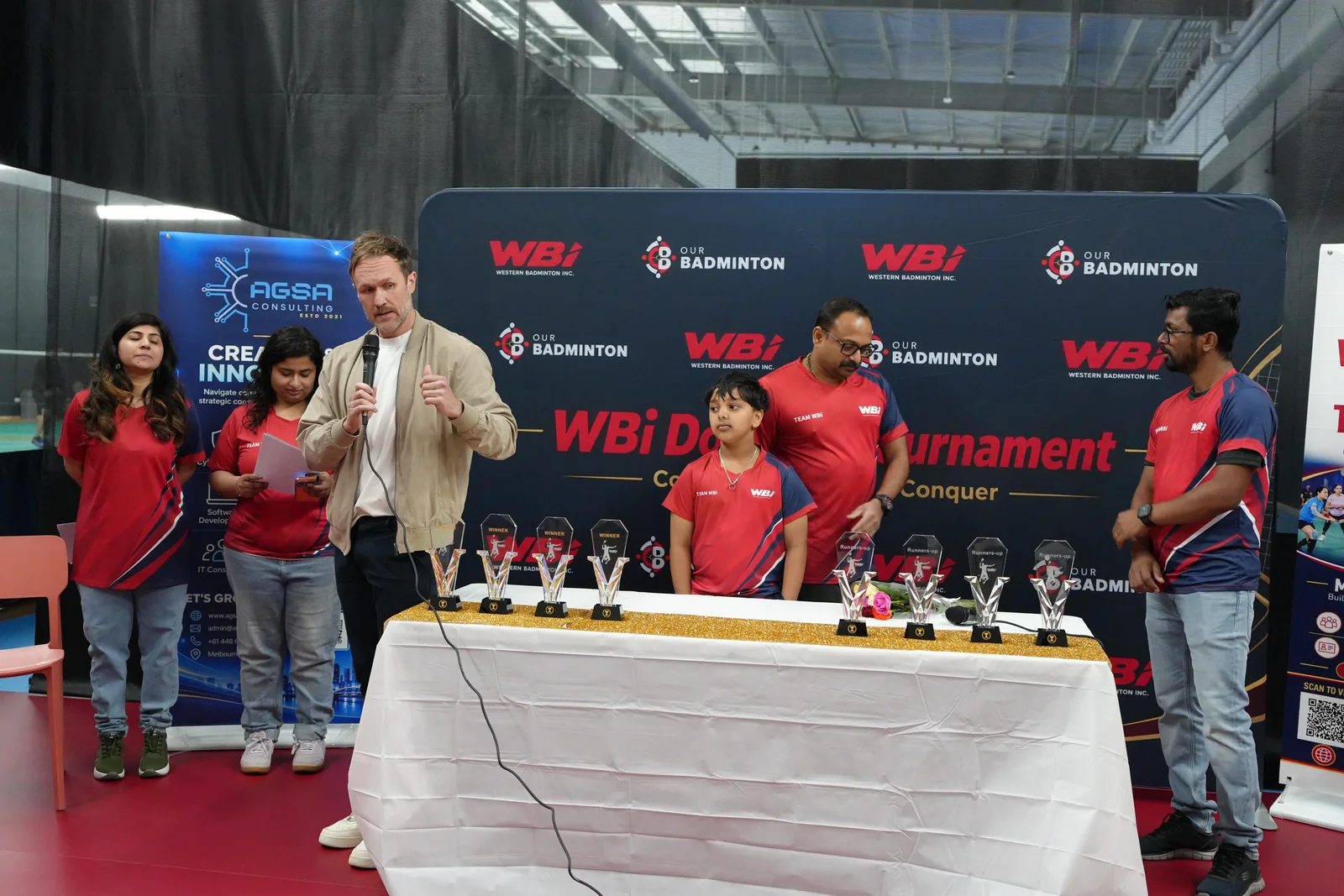Clint Proctor addressing the community beside Team WBi and the tournament trophies